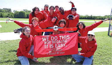 Group of people in red hoodies holding a red banner with white text.