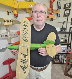 Man holding a green model airplane in a room filled with similar models.