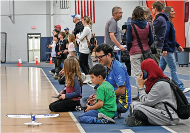 People watching and controlling toy planes in a gymnasium.