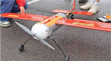Red model airplane on asphalt, person adjusting the wing.