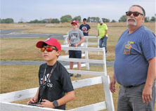 Boys and adults controlling models outdoors, wearing sunglasses.