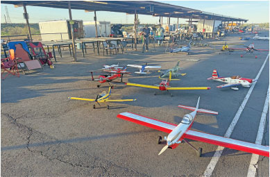 Toy airplanes on an airstrip under a shaded area, with people in the background.