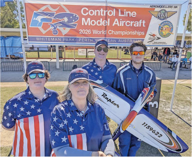 Four people in star-and-stripe shirts hold a model aircraft in front of a championship banner.