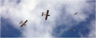 Four small planes flying in a cloudy blue sky.