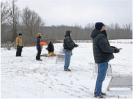 Five people flying drones in a snowy field.