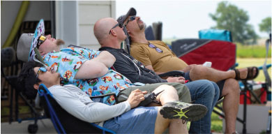 Four people relaxing in folding chairs, looking up, outdoors on a sunny day.