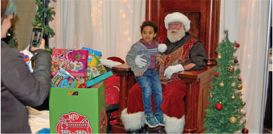 Child sitting with Santa, surrounded by Christmas decorations and gifts.