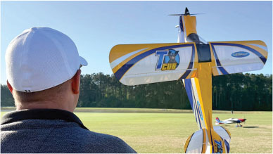 Man in white cap flying RC airplane with "TX Cub" design.