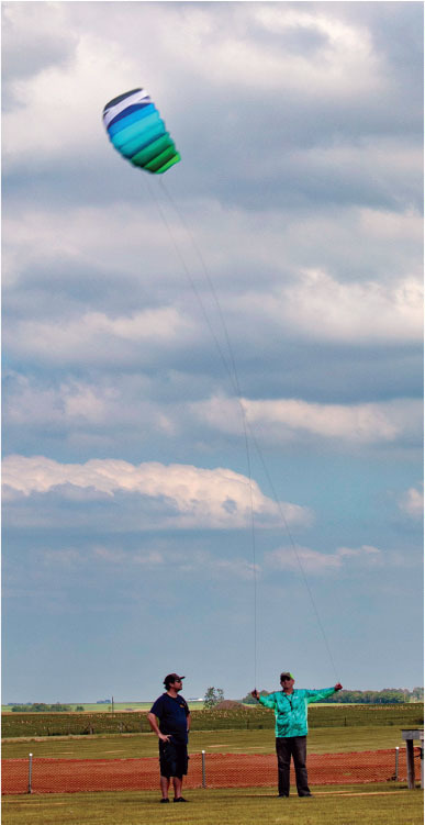 Two people flying a colorful kite in an open grassy field under a cloudy sky.