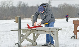Person in winter clothes adjusting a red model airplane on a snowy field.