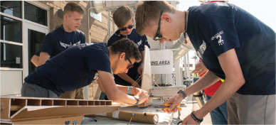 Students assembling a model outdoors, wearing matching navy shirts.