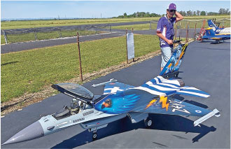 Model jet with blue and gray design on a tarmac, man standing beside.