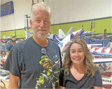 Man and woman smiling in front of model airplanes in a gym.