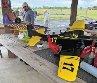 Two colorful model airplanes on a wooden table, with people in the background.