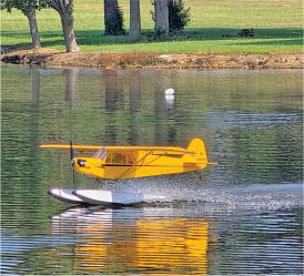 Yellow seaplane landing on a calm lake.