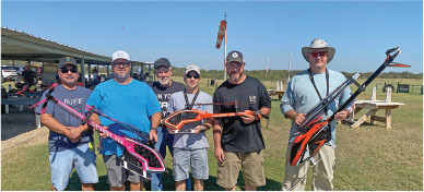 Men outdoors holding colorful model helicopters, smiling under a clear sky.