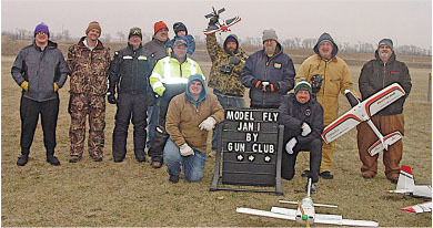 Group of people in winter clothes outside with model planes and a sign that reads "Model Fly Jan."