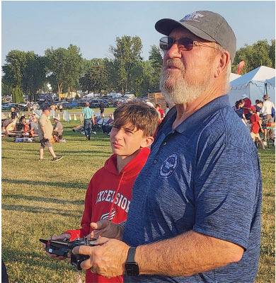 Man and boy operating drone controls at outdoor event.