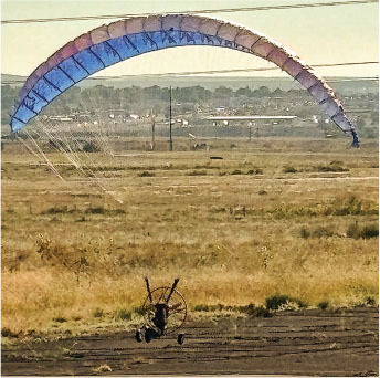 Paramotor with colorful parachute on a field.