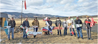 People holding model airplanes stand in a grassy field.