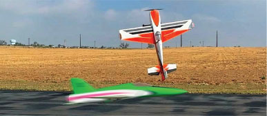 Toy planes flying and landing in a grassy field, one orange and one green.