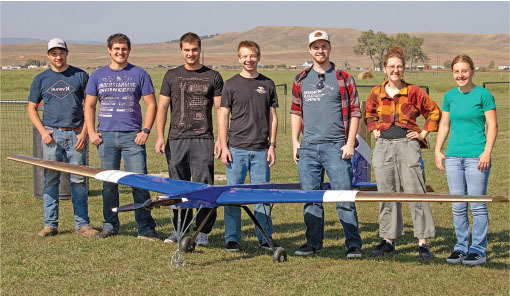 Seven people standing on grass with a model aircraft in front.