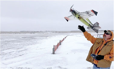 Man in winter clothes launching a small model aircraft in a snowy field.
