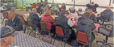 People gathered indoors at tables with red cups and checkered tablecloths.