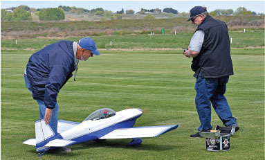Two men with a remote-controlled model plane on a grassy field.