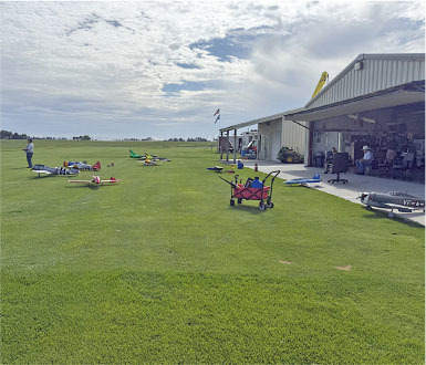 Model airplanes on grass field near a hangar under a cloudy sky.