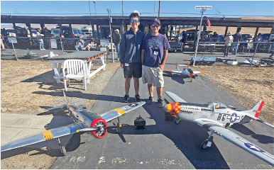 Two people with remote-controlled model planes on a sunny day.