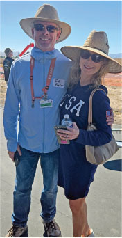 Two people wearing sunglasses and hats, smiling outdoors under a blue sky.