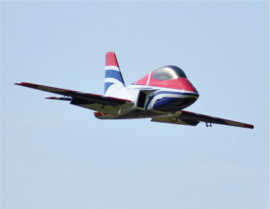 Red and blue model jet with white stripes flying in clear sky.