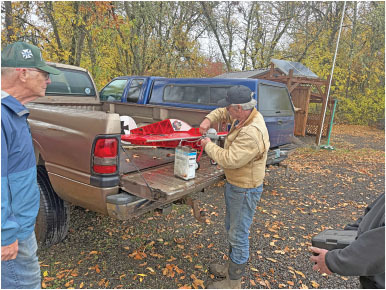 Man adjusting a red model aircraft on a truck's tailgate, surrounded by autumn trees.