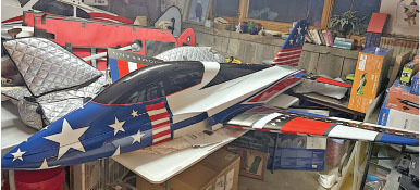 Model airplane with stars and stripes in a cluttered workshop.