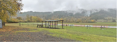 Rural landscape with grass, covered picnic area, and distant foggy hills.