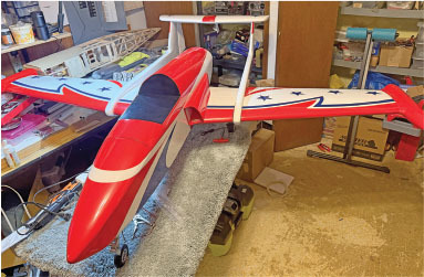 Red and white model airplane with stars, in a cluttered workshop.