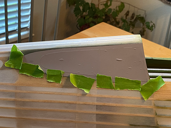 Gray wing model on a table with green tape and blurred indoor plants.