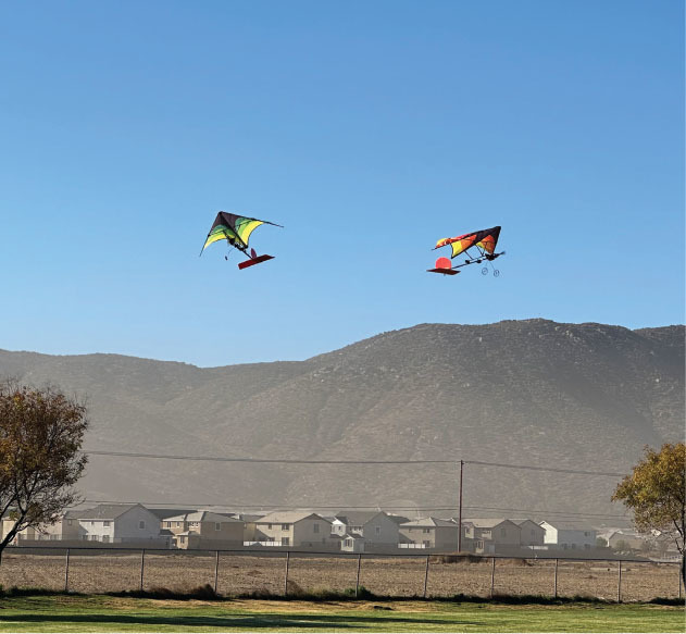 Two colorful kites flying above houses with mountains in the background.