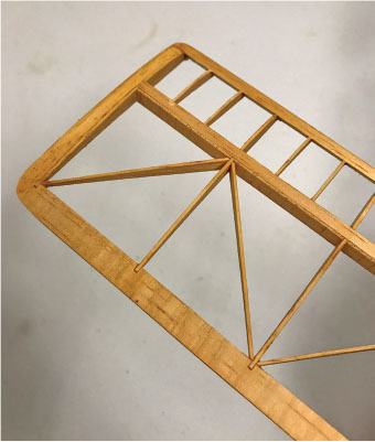 Wooden model airplane wing skeleton on a beige surface.