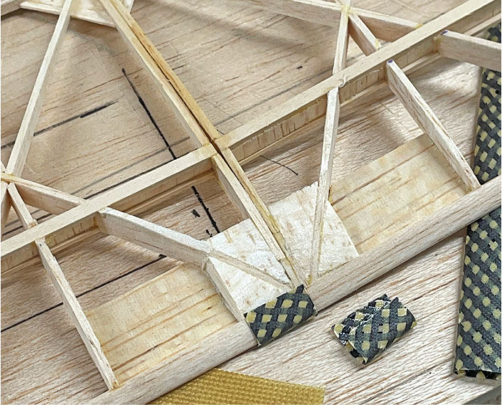 Wooden model structure with patterned fabric swatches on a wooden surface.