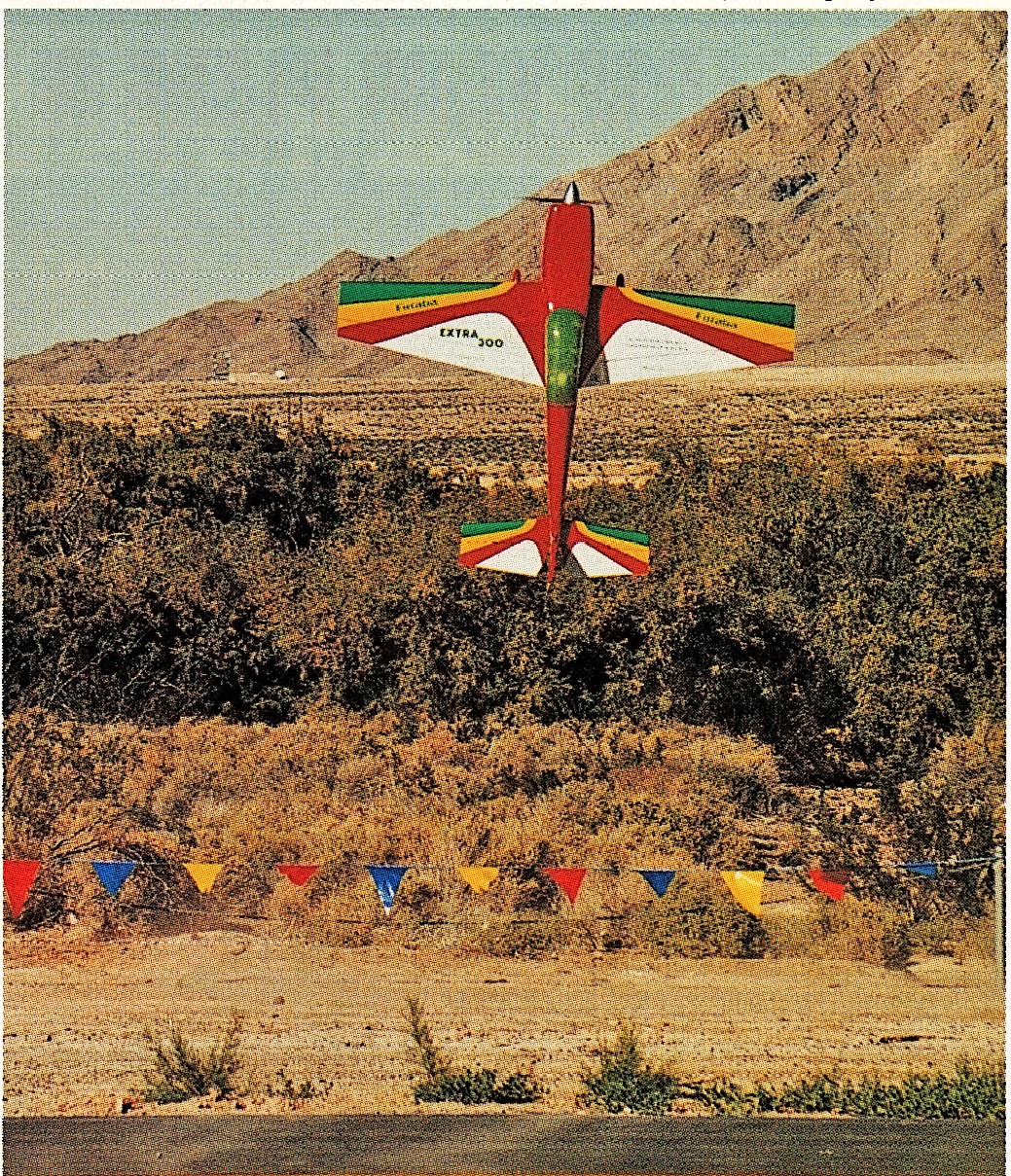 Stunt plane flying vertically near desert mountains, colored flags below.
