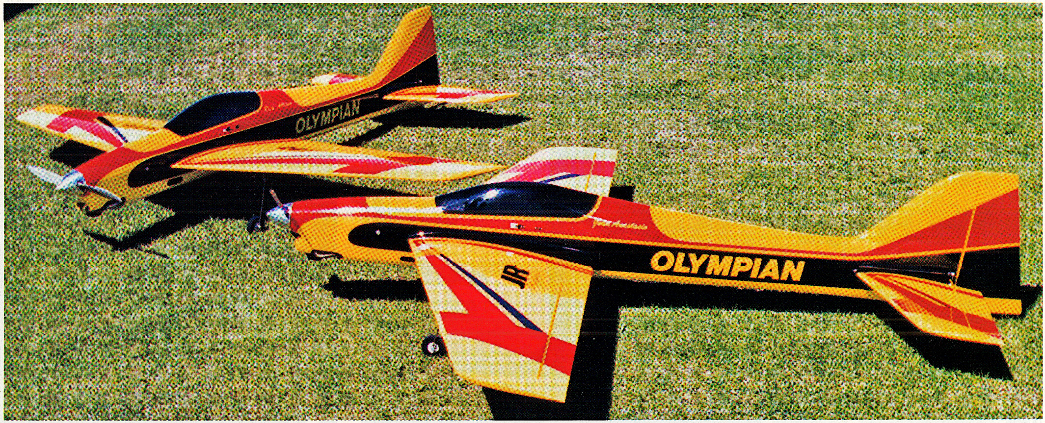Two model airplanes on grass, marked "OLYMPIAN," in red, yellow, and black.