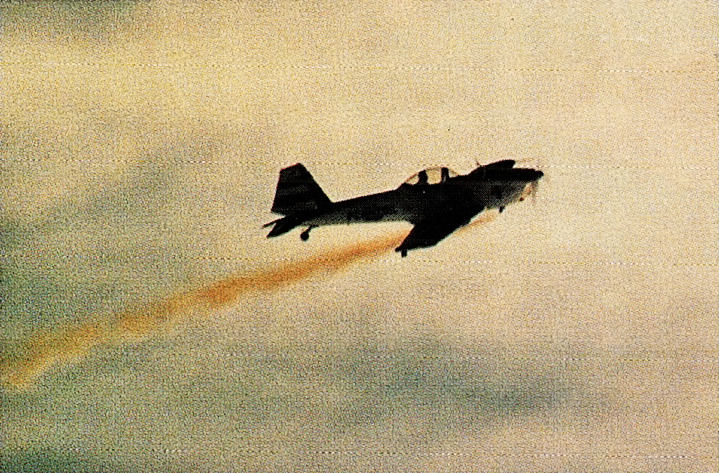 Single propeller plane flying, trailing orange smoke.