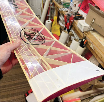 Model airplane wing with red and yellow geometric design, held in a workshop.