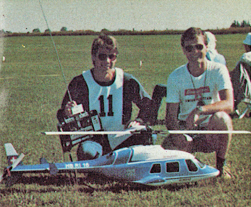 Two people kneeling on grass with a model helicopter.