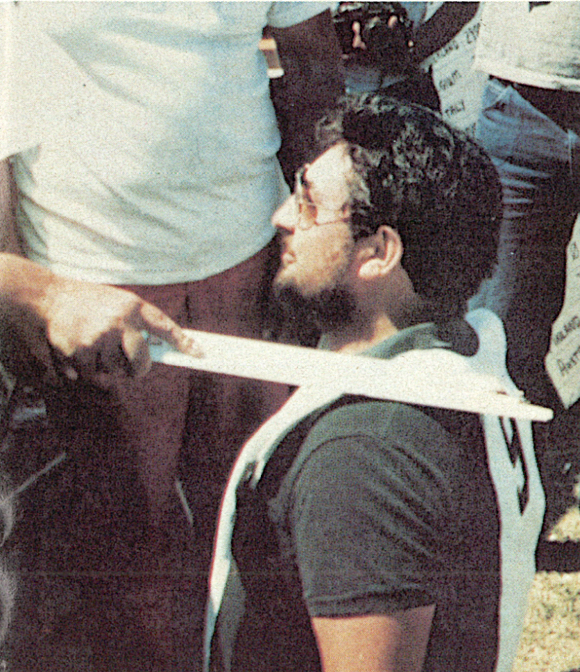 Man kneeling with a sword on his back, surrounded by people.