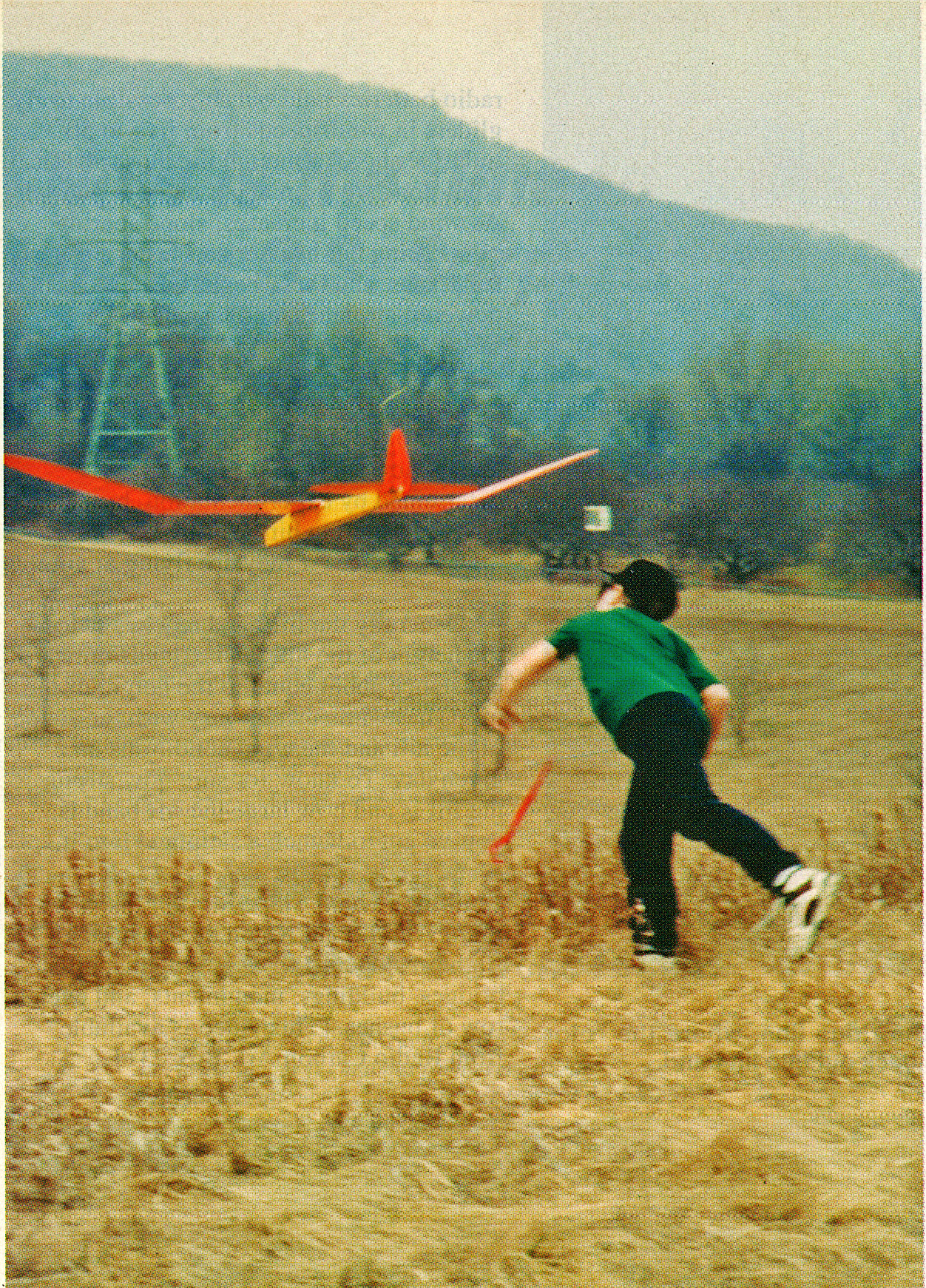 Boy in a field launching a red and yellow model glider.