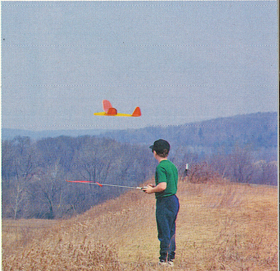 Boy flying a red toy plane in a grassy field.