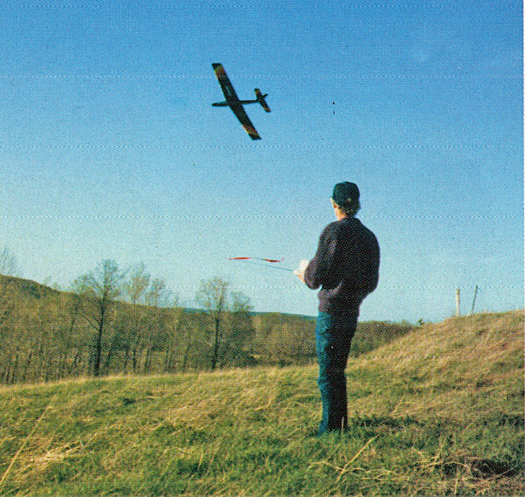 Man flying model plane outdoors on a grassy hill.